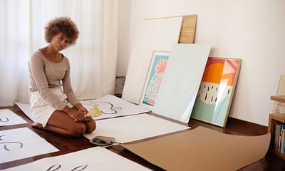 young artist sitting on floor with artworks
